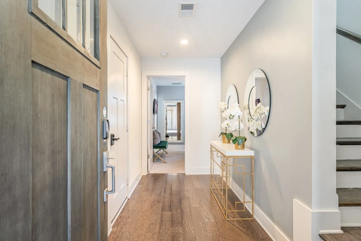 An inviting view of the entryway with a front door, decorative mirrors, and a console table topped with flowers. The scene is warm and set to welcome guests of all ages.