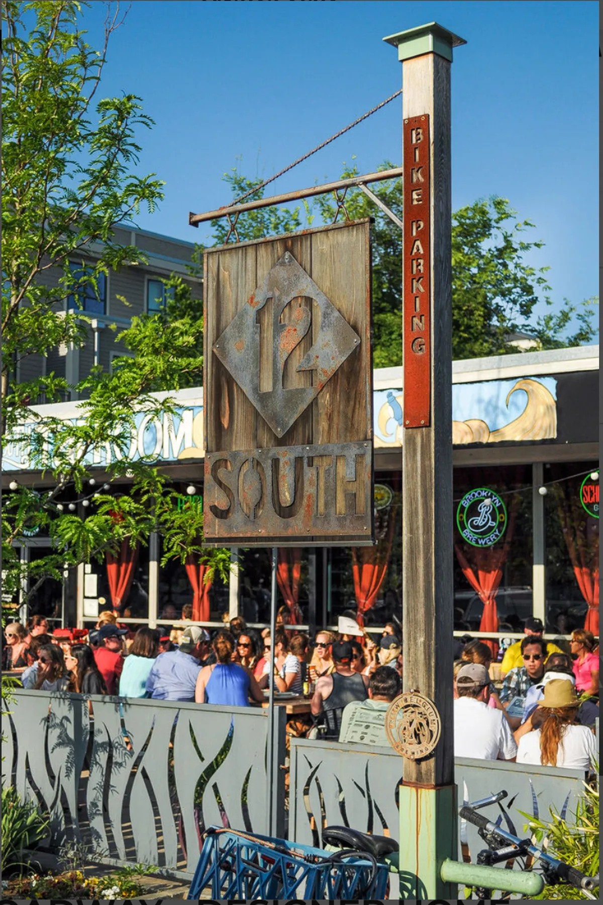 This exterior shot captures the vibrant 12 South neighborhood, with the iconic '12 South' sign, people dining outdoors at bustling restaurants, and details like bike parking and lively street life. The image exudes energy and community, perfectly capturing the trendy, walkable atmosphere described in the section.